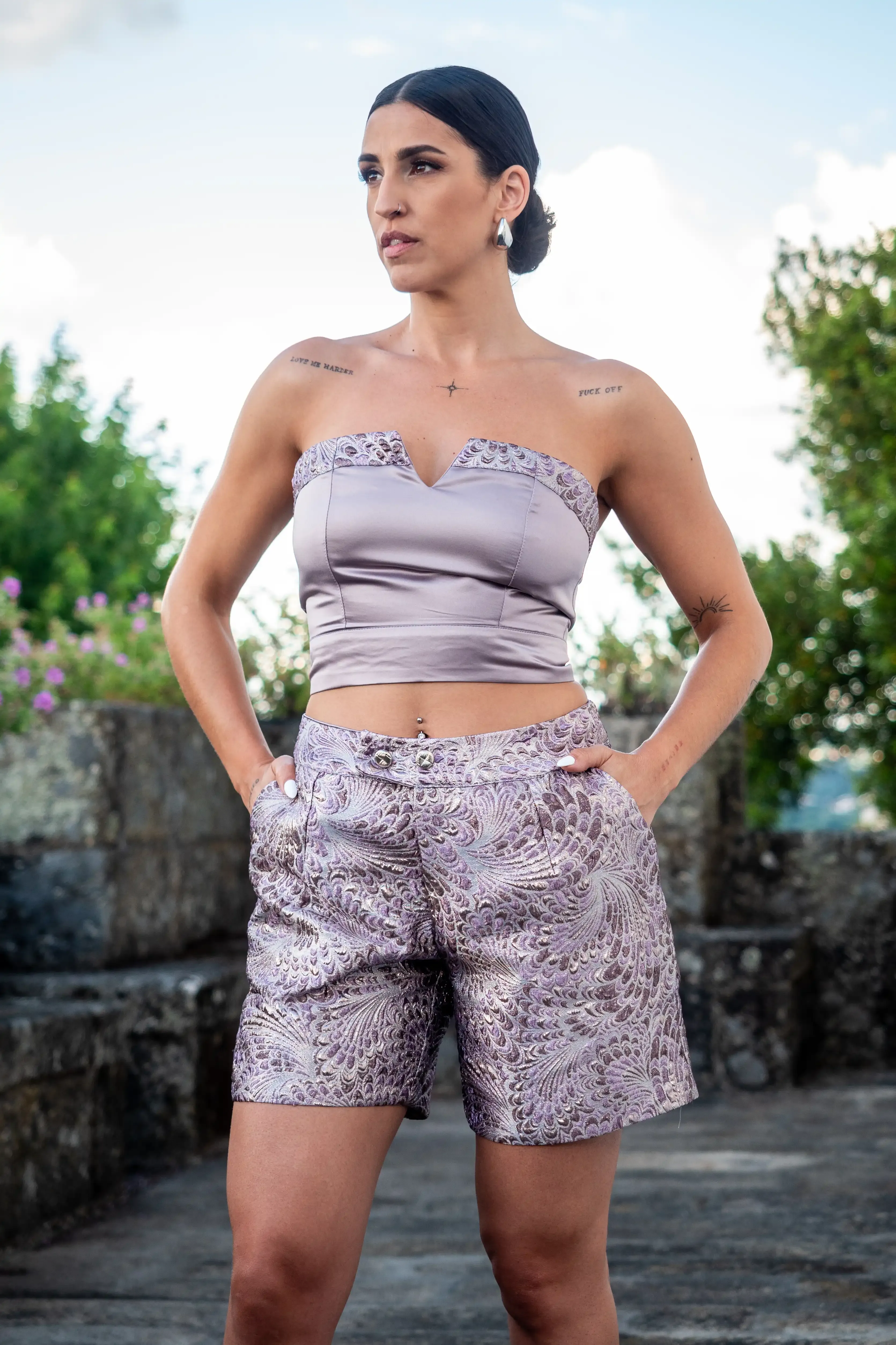 Uma mulher está a posar com calções e um crop top sem mangas de cor-de-rosa metálico. Os calções têm um padrão orgânico em relevo.